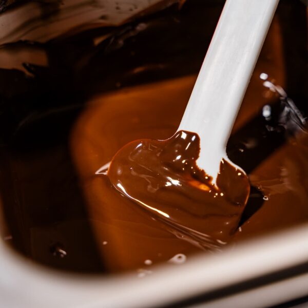 Nahaufnahme von einem Spatel, der in dunkle Schokolade getaucht wird.